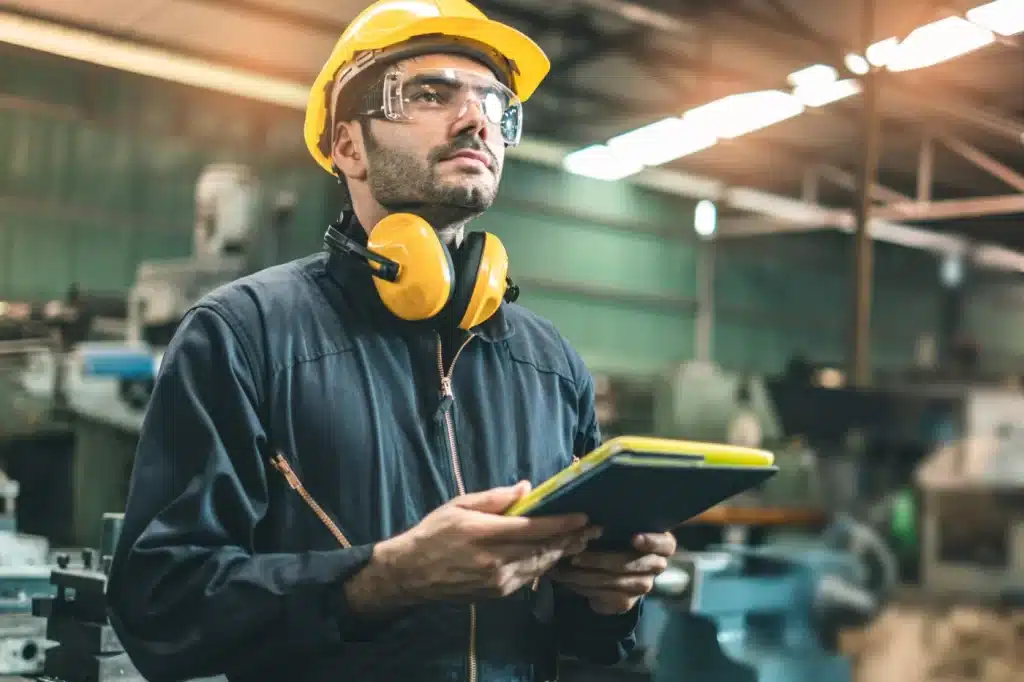 Engineer in a hard hat and safety glasses reviewing documentation on a tablet in a factory